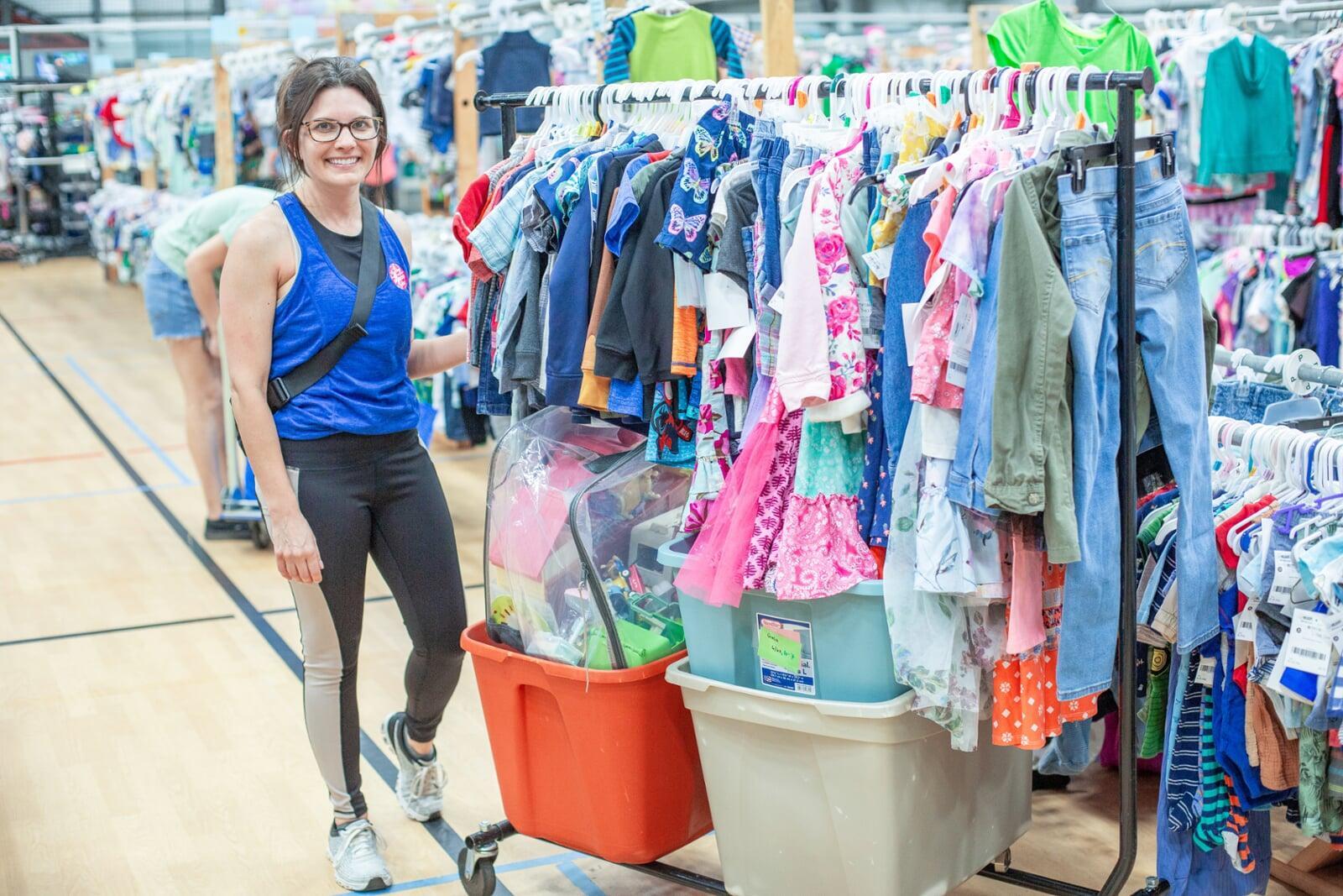A JBF Team Member wears a black JBF apron while organizing infant clothing on the clothing racks.